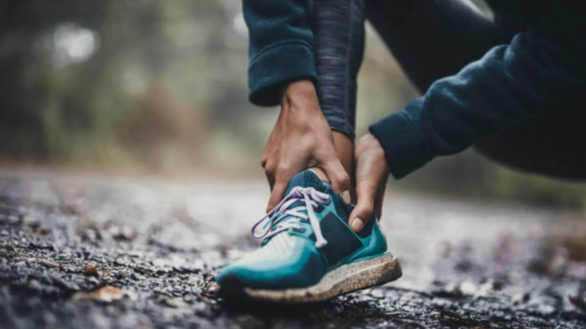A runner is feeling their ankle and foot to check for any pain points.