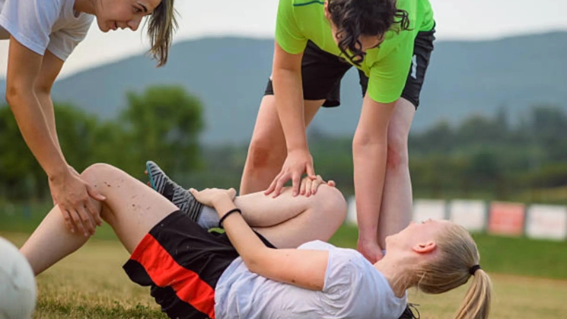 A young footballer has a sports injury and is being helped by her teammates.